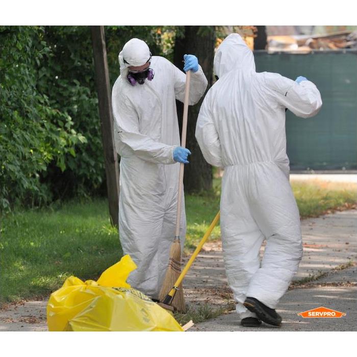 two men in white hazmat suits outside raking things into a bag